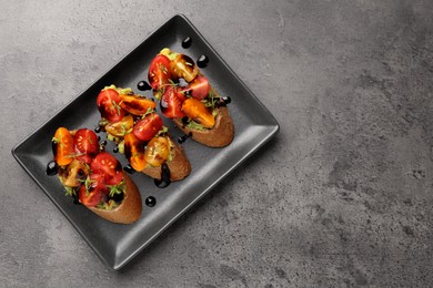 Photo of Delicious bruschettas with avocado, tomatoes and balsamic vinegar on gray textured table, top view. Space for text