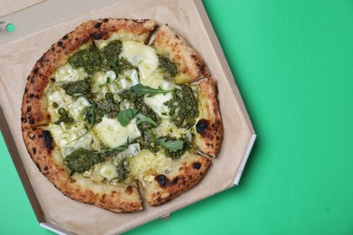 Delicious pizza with pesto, cheese and arugula in cardboard box on green background, top view