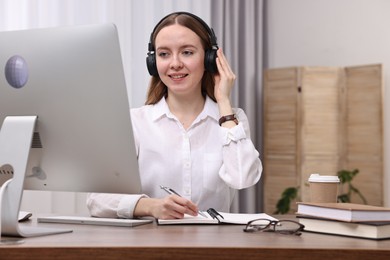 E-learning. Young woman taking notes during online lesson at wooden table indoors