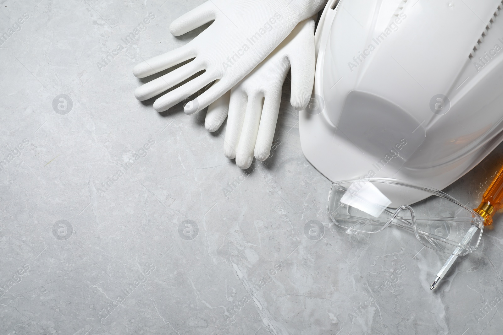 Photo of Hard hat, protective gloves, goggles and screwdriver on grey surface, flat lay. Space for text