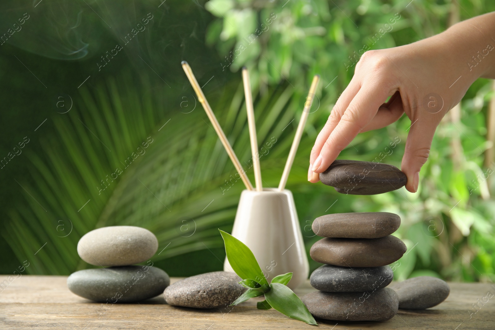 Photo of Woman stacking stones on table against blurred background, closeup. Zen concept