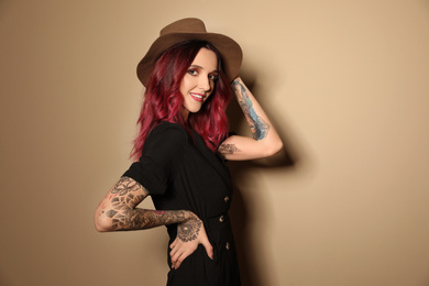 Beautiful woman with tattoos on arms against beige background