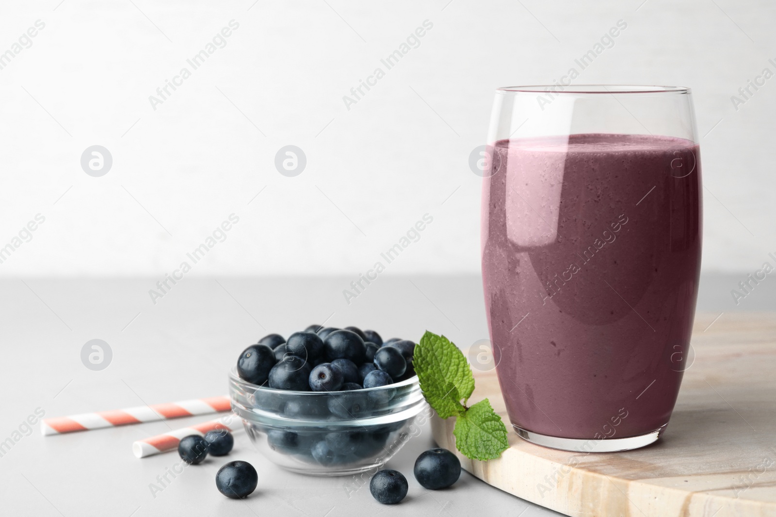 Photo of Fresh acai drink with berries on grey table against light background. Space for text