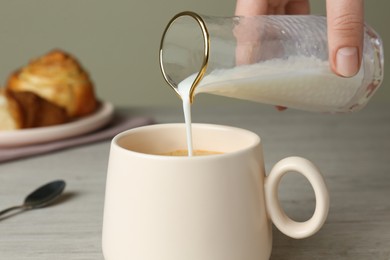 Photo of Woman pouring milk into cup of coffee at table, closeup