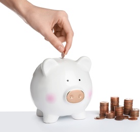 Photo of Woman putting coin into piggy bank on white background, closeup