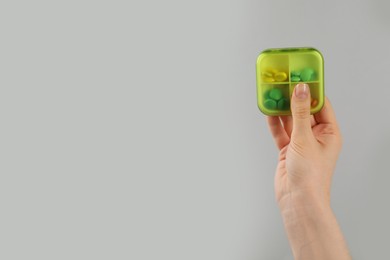 Photo of Woman holding plastic box with different pills on light grey background, closeup. Space for text