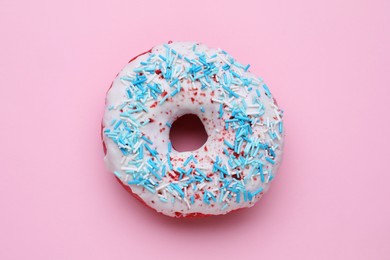 Photo of Glazed donut decorated with sprinkles on pink background, top view. Tasty confectionery