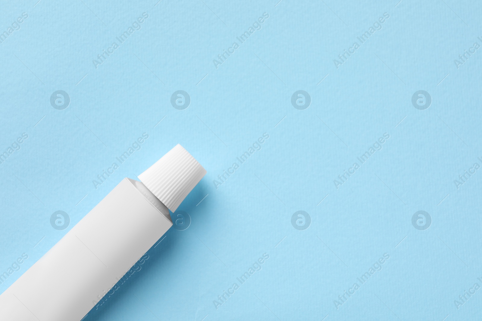 Photo of Tube of ointment on light blue background, top view. Space for text