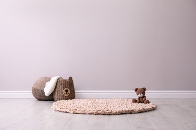 Toy bear and wicker basket near light grey wall in child room. Interior design