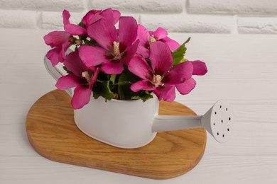 Beautiful flowers in watering can on white wooden table near brick wall