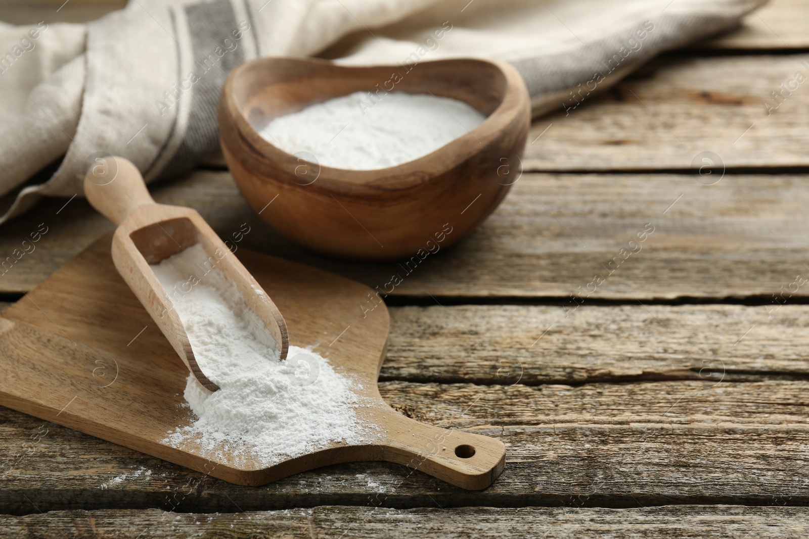 Photo of Baking powder in scoop and bowl on wooden table, closeup. Space for text