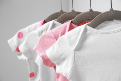 Photo of Hangers with baby bodysuits on white background, closeup