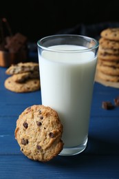 Photo of Tasty chocolate chip cookies and glass of milk on blue wooden table