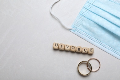 Photo of Flat lay composition with protective mask and wedding rings on light grey background, space for text. Divorce during coronavirus quarantine