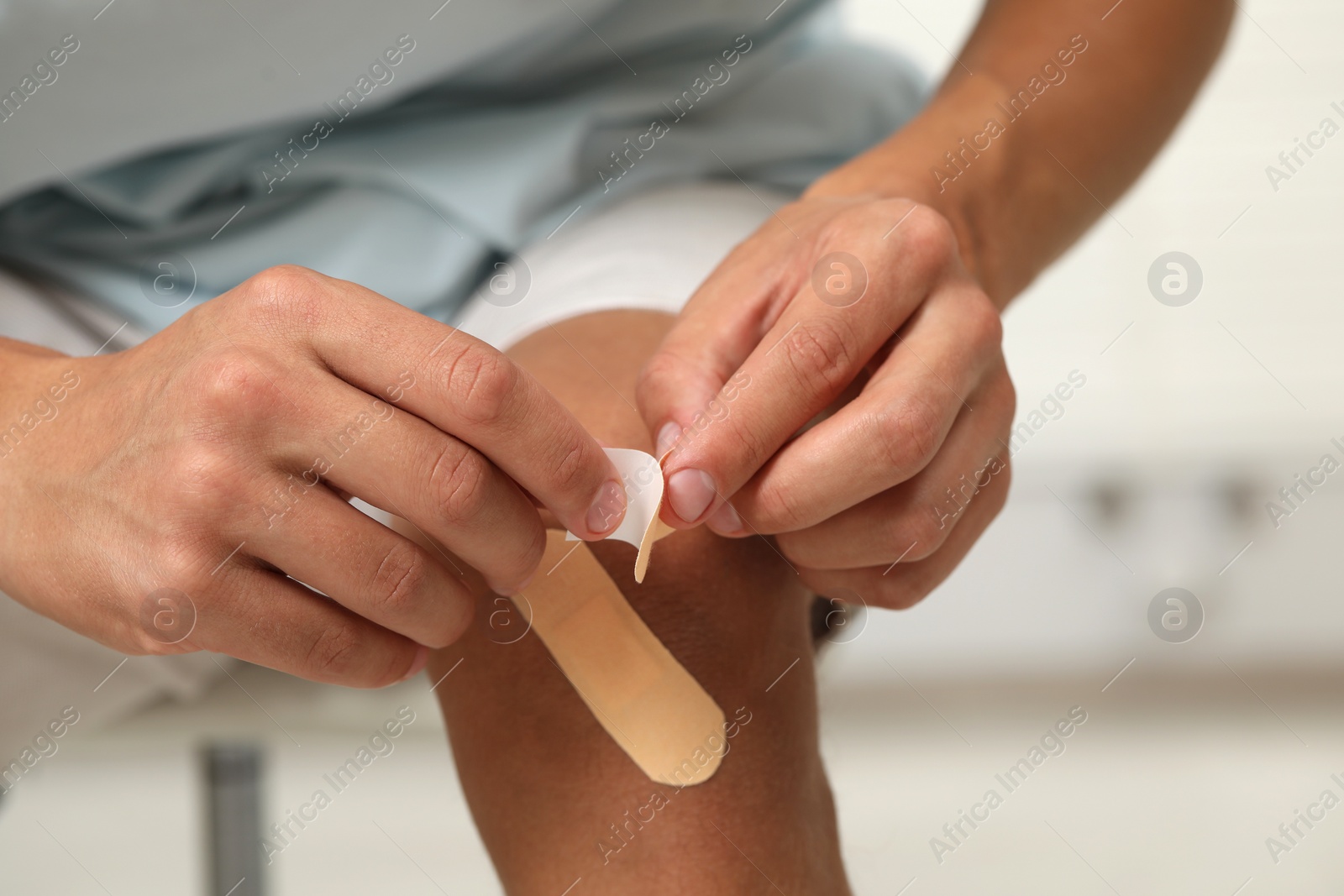 Photo of Man putting sticking plasters onto knee indoors, closeup