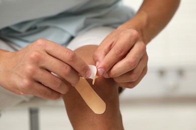 Photo of Man putting sticking plasters onto knee indoors, closeup