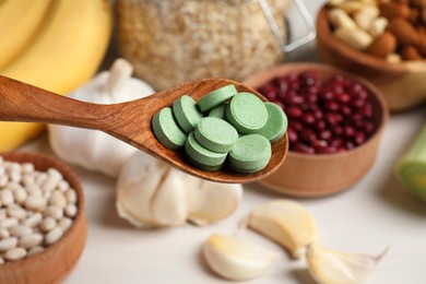 Photo of Holding spoon of prebiotic pills near table with food, closeup