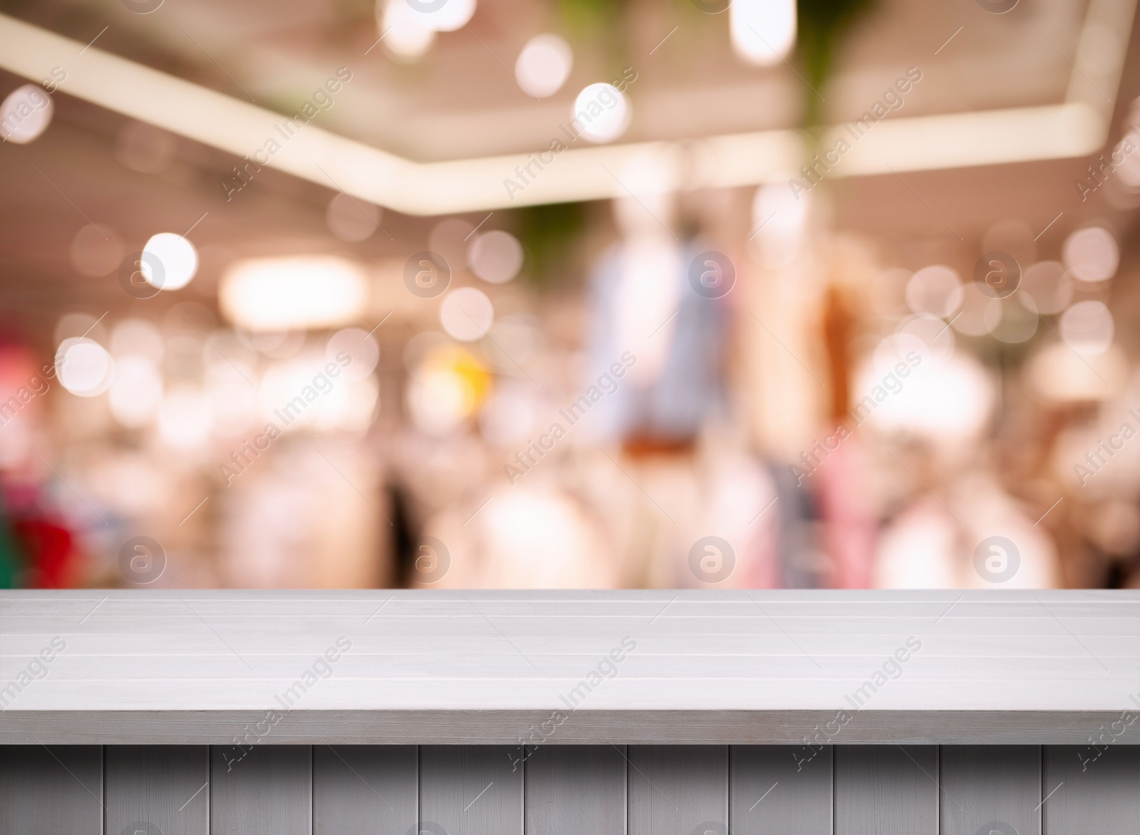 Image of Empty white wooden surface and blurred view of clothes store interior. Space for design