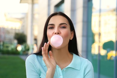 Photo of Beautiful woman blowing gum near building outdoors