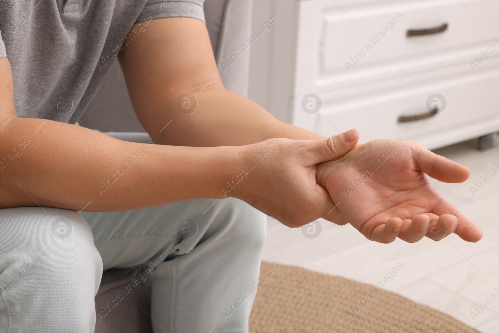 Photo of Man suffering from pain in his hand on armchair indoors, closeup