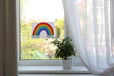Photo of Picture of rainbow on window and houseplant indoors. Stay at home concept