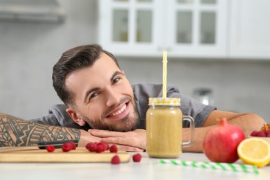 Photo of Handsome man with delicious smoothie and ingredients at white table in kitchen