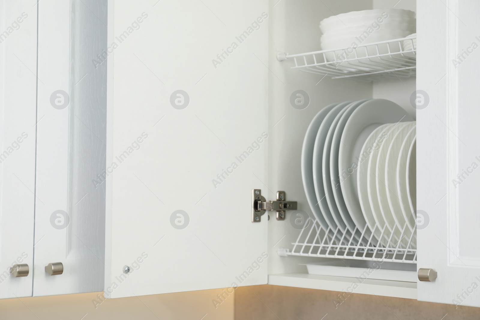 Photo of Clean plates and bowls on shelves in cabinet indoors