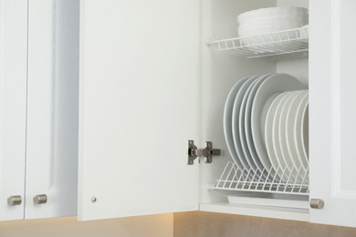 Photo of Clean plates and bowls on shelves in cabinet indoors