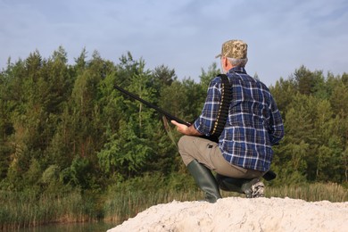 Man with hunting rifle near lake outdoors, back view. Space for text