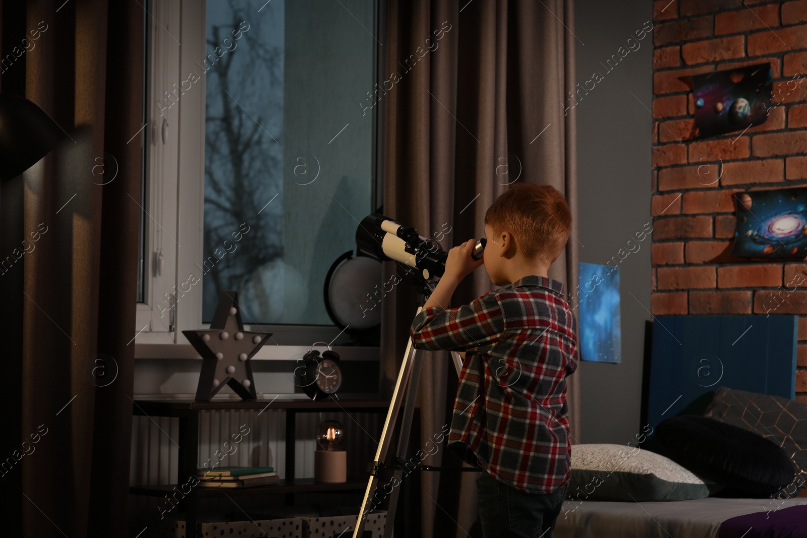 Photo of Little boy looking at stars through telescope in room, back view