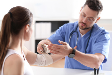 Photo of Male orthopedist applying bandage onto patient's elbow in clinic