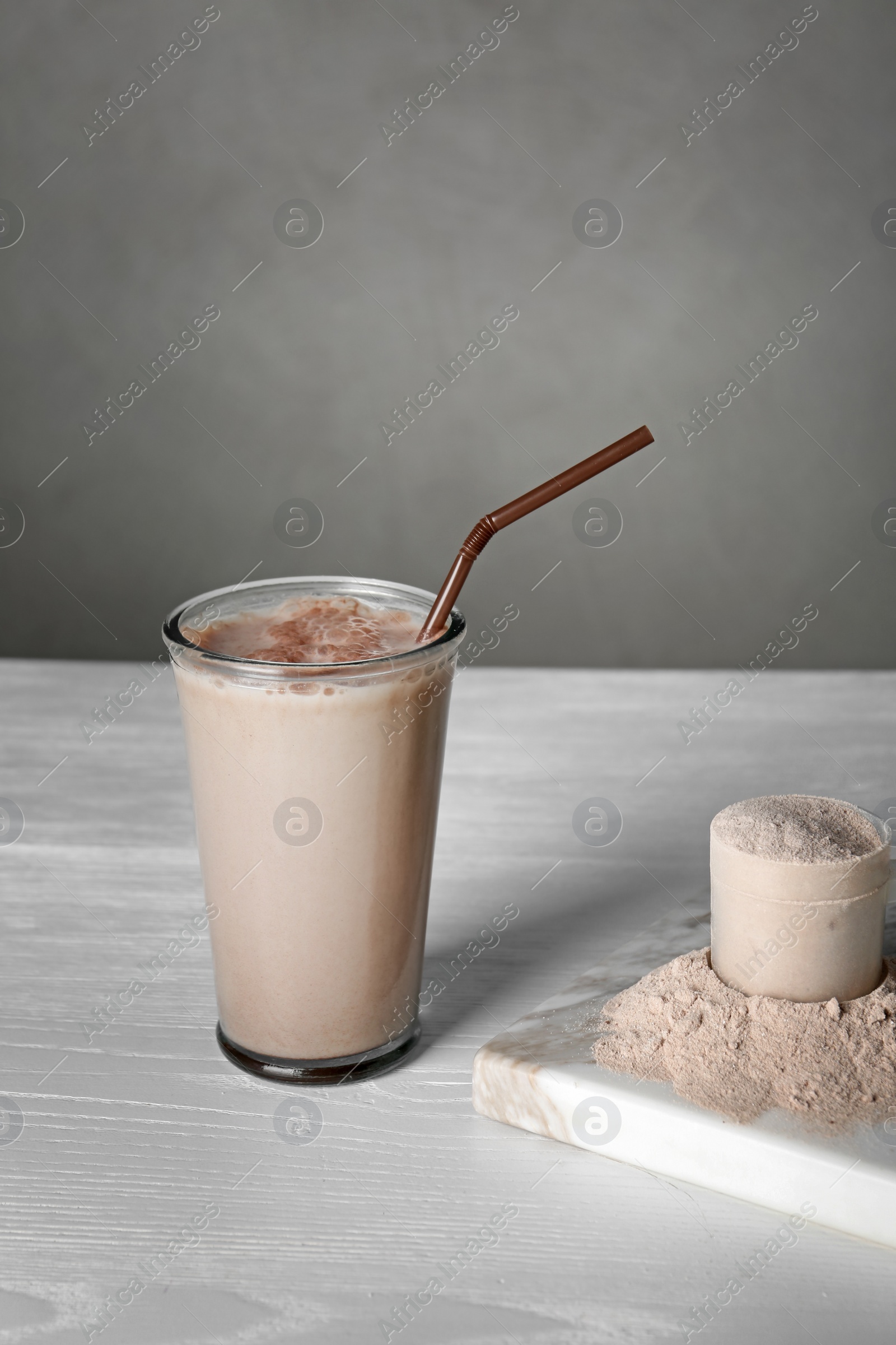 Photo of Glass with protein shake and scoop of powder on white wooden table. Space for text