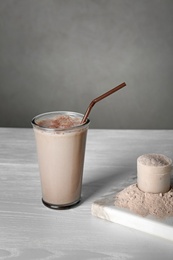 Photo of Glass with protein shake and scoop of powder on white wooden table. Space for text