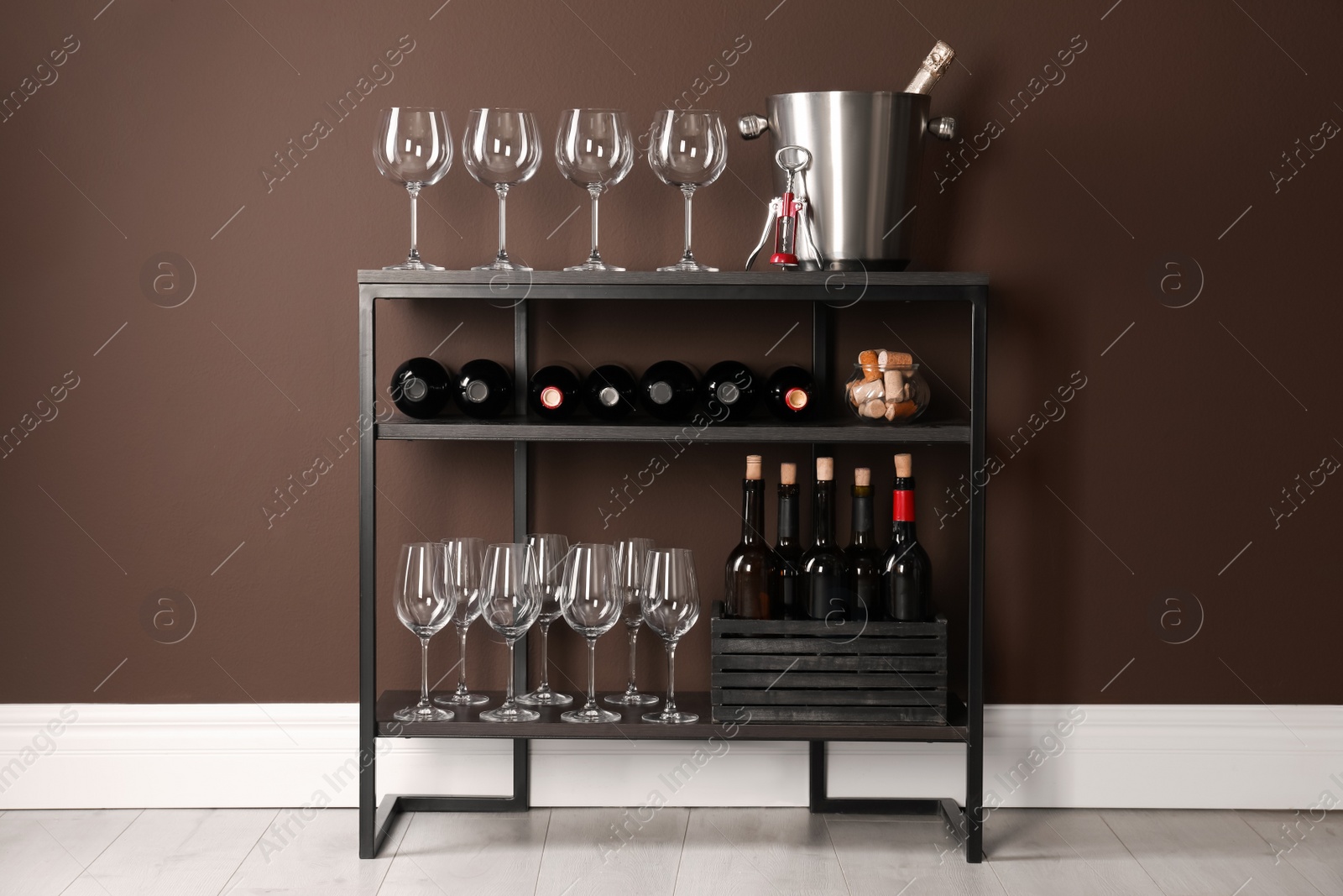 Photo of Rack with bottles of wine and glasses near brown wall