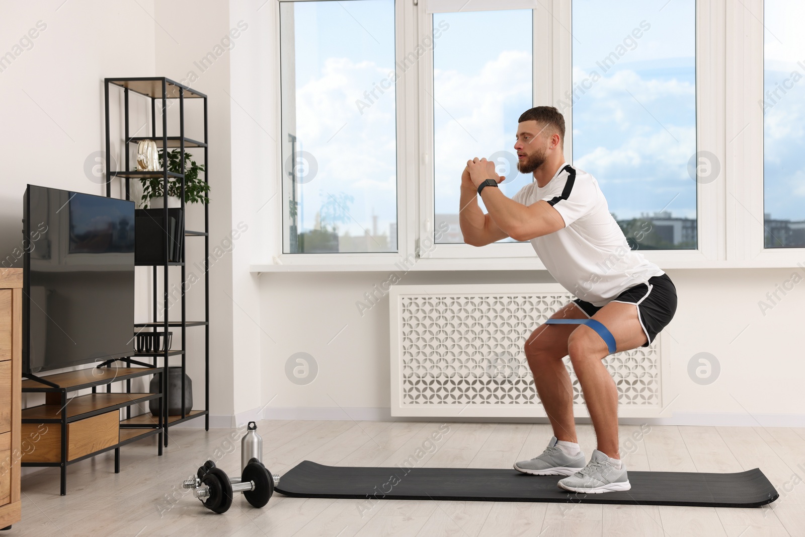 Photo of Athletic man doing exercise with elastic resistance band on mat at home