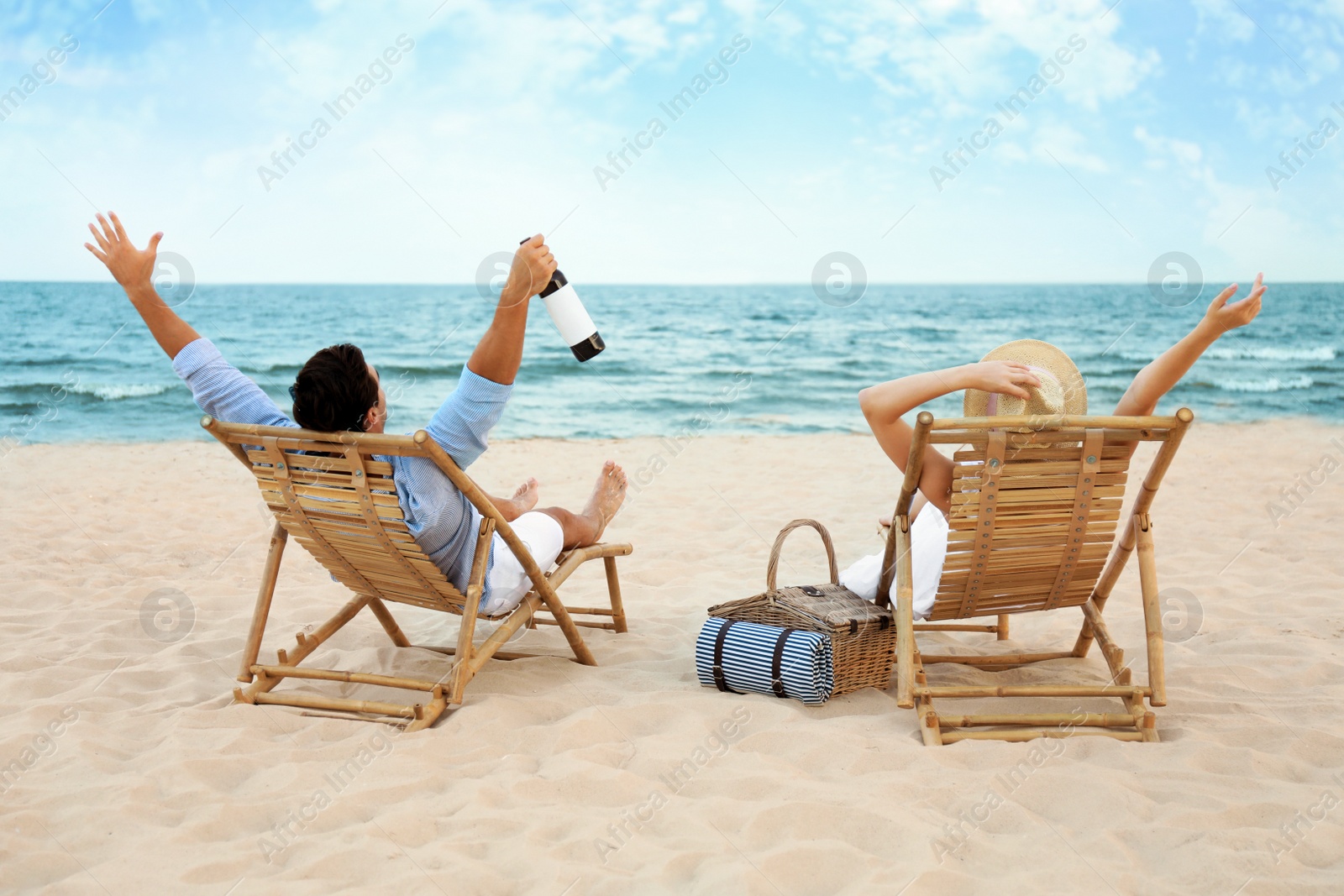Photo of Happy young couple with wine sitting on deck chairs at sea beach