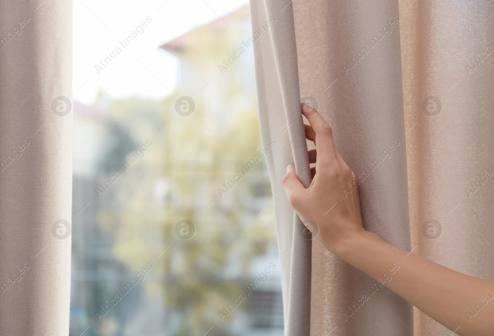 Photo of Woman opening window curtains at home, closeup. Space for text