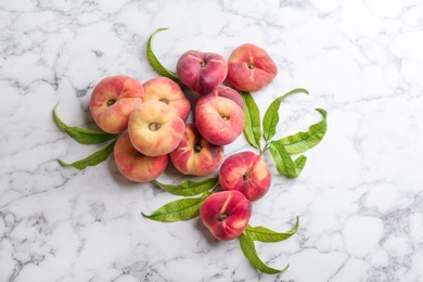 Photo of Fresh ripe donut peaches with leaves on white marble table, flat lay