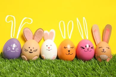 Image of Colorful eggs as Easter bunnies on green grass against yellow background