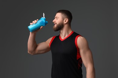 Photo of Young man with muscular body holding shaker of protein on grey background