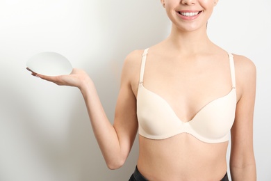 Photo of Woman holding silicone implant for breast augmentation on white background, closeup. Cosmetic surgery