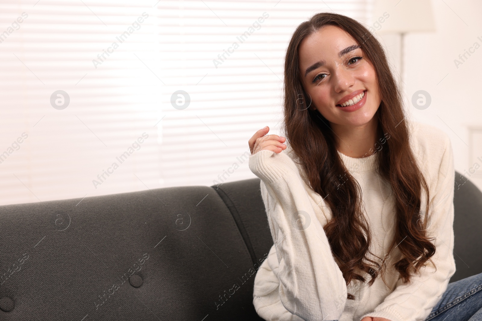 Photo of Beautiful young woman in stylish warm sweater on sofa at home, space for text