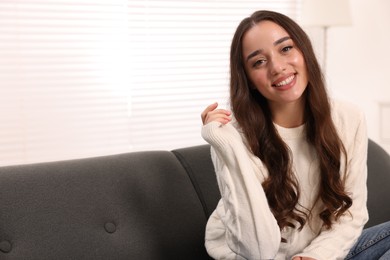 Beautiful young woman in stylish warm sweater on sofa at home, space for text