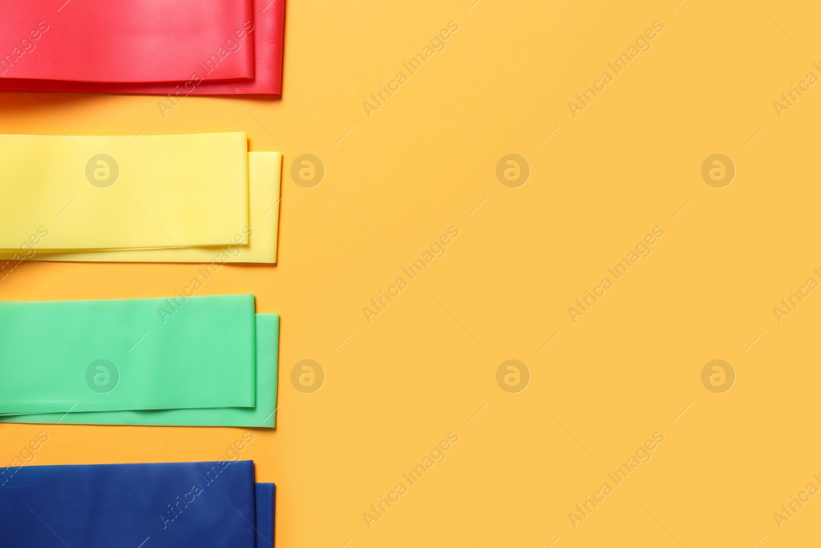 Photo of Set of colorful fitness elastic bands on orange background, flat lay. Space for text