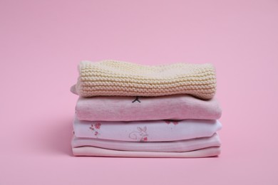 Stack of clean baby clothes on pink background