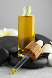 Photo of Bottle of face serum with spa stones and beautiful flowers on light grey table, closeup