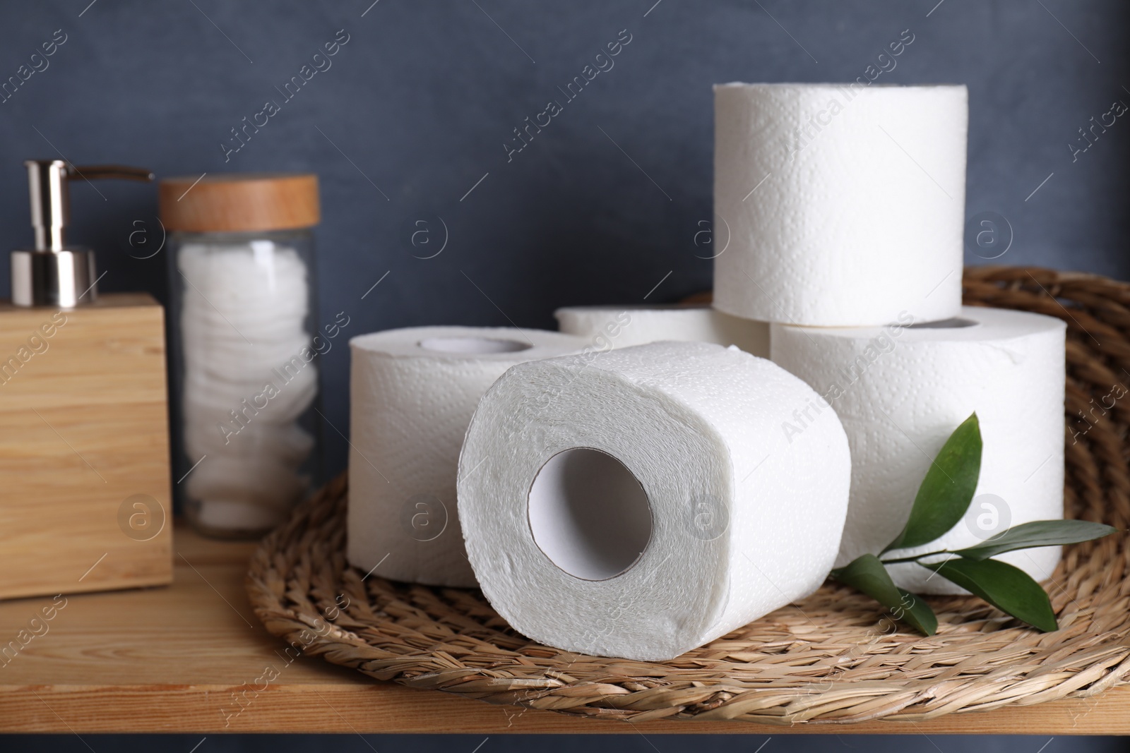 Photo of Toilet paper rolls, green leaves, dispenser and cotton pads on wooden table