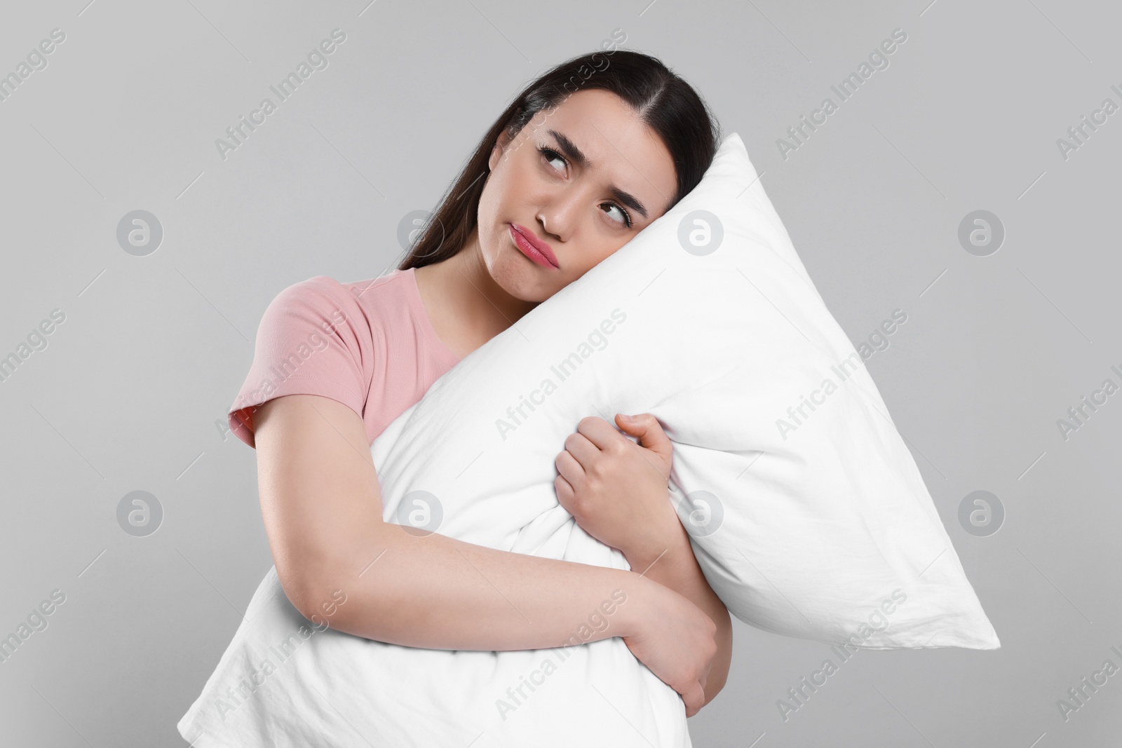 Photo of Tired young woman with pillow on light grey background. Insomnia problem