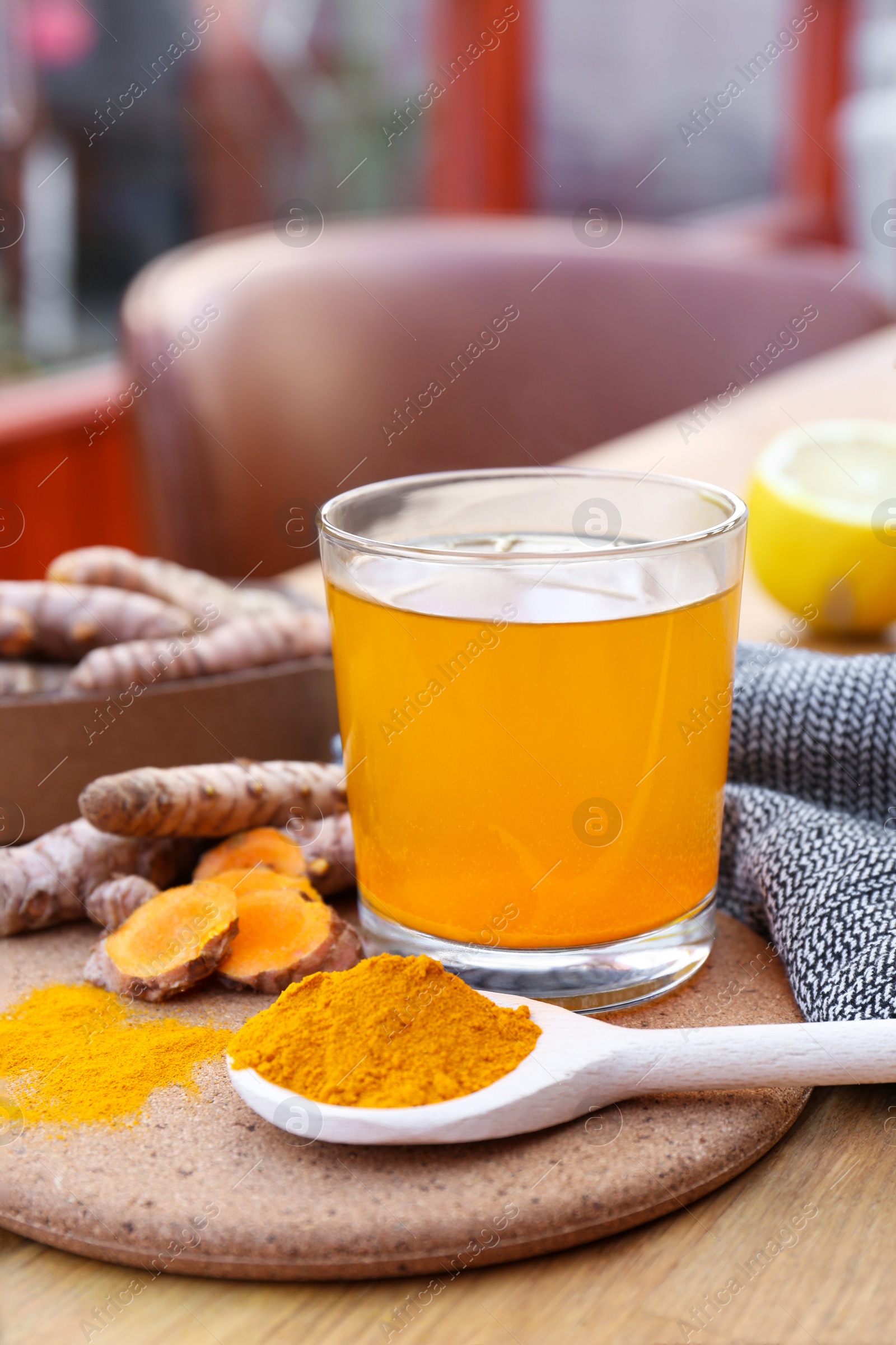 Photo of Glass cup of hot tea, lemon, turmeric powder and roots on wooden table