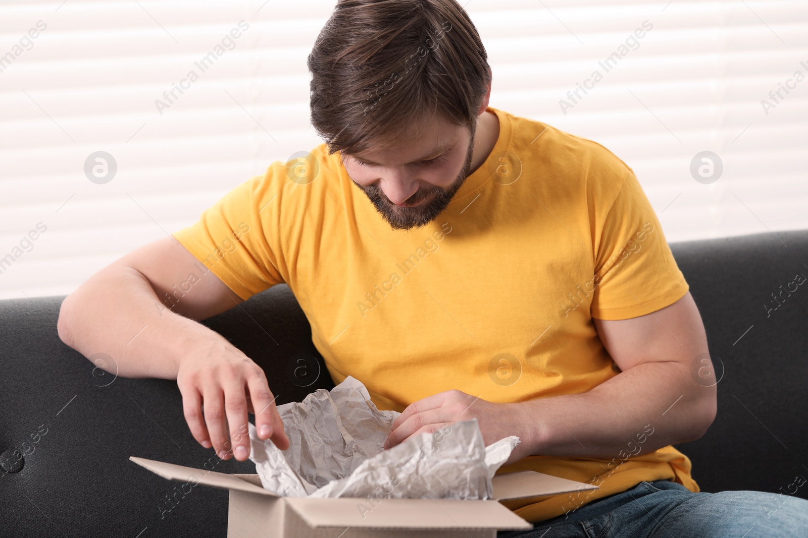 Photo of Man opening parcel at home. Internet shopping